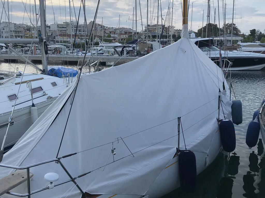 A sailing yacht in a marina under a full pale grey winter cover
