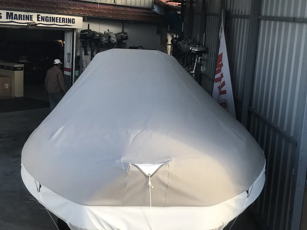 A RIB under a fitted white cover, stored inside the workshop