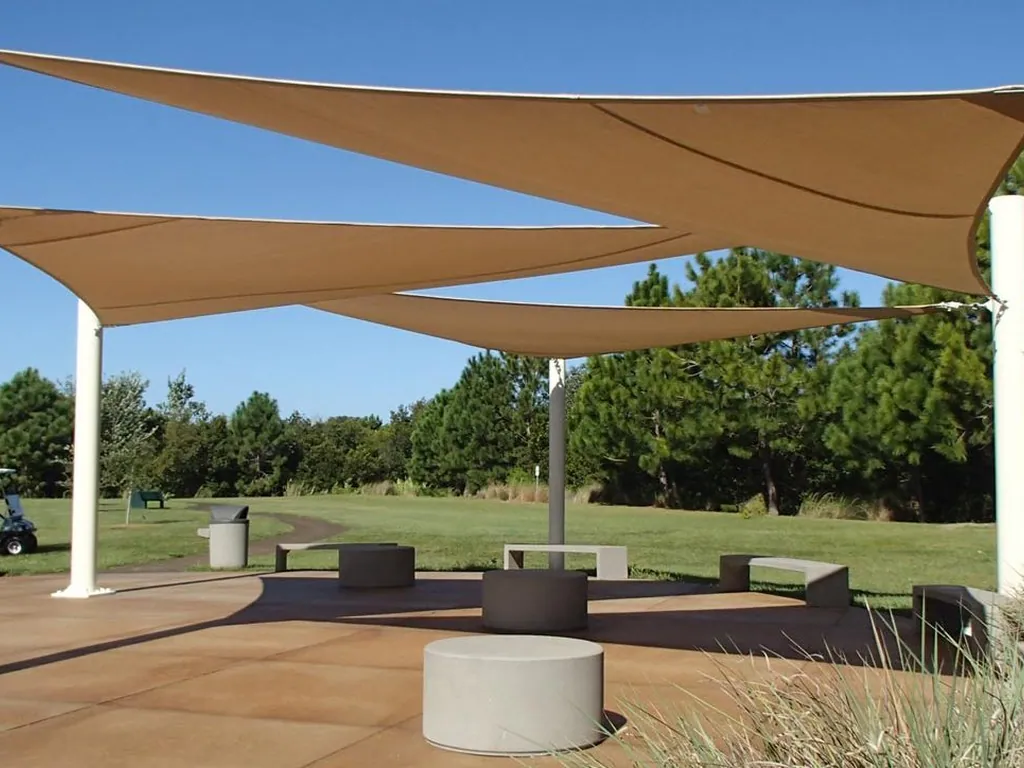 Tan shade sails on tall masts over an open lawn
