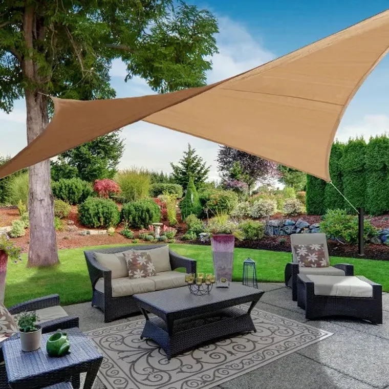 Tan shade sail over a garden lounge, lawn and planting behind