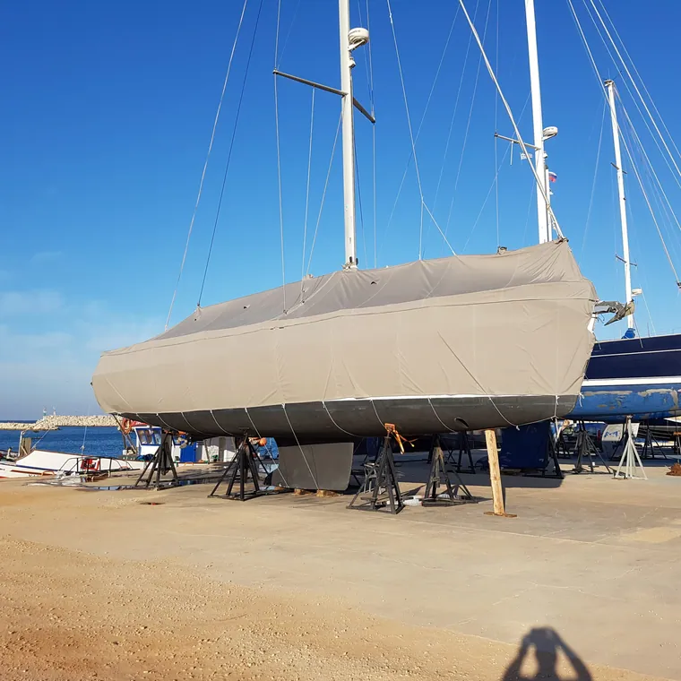 Sailing yacht ashore in the boatyard under a full cover, hull propped on stands