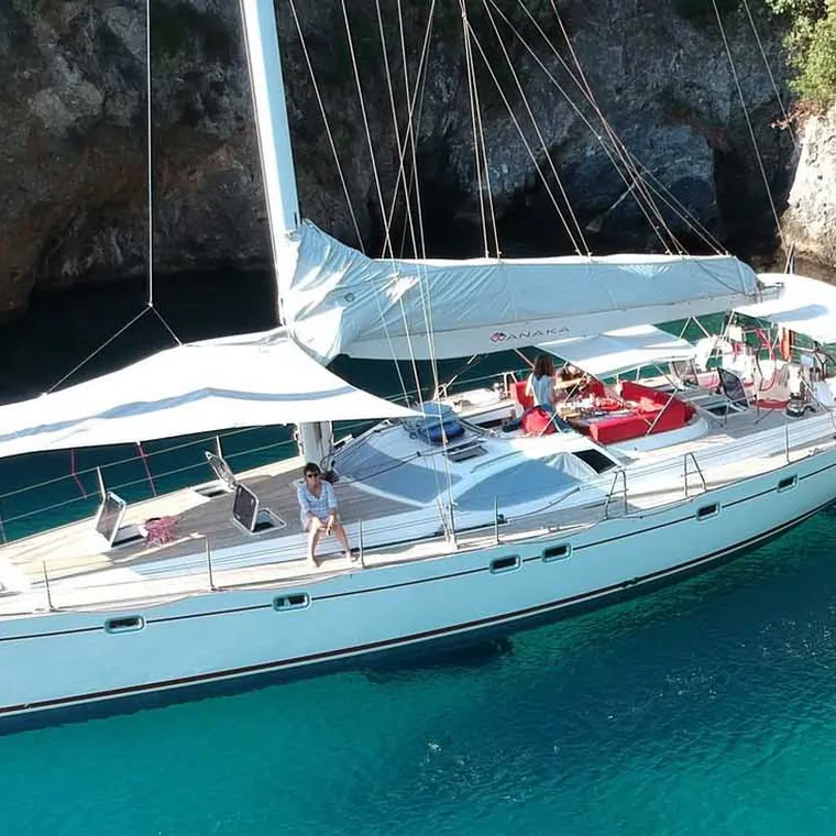 Large sailing yacht at anchor in a turquoise cove under a white shade sail