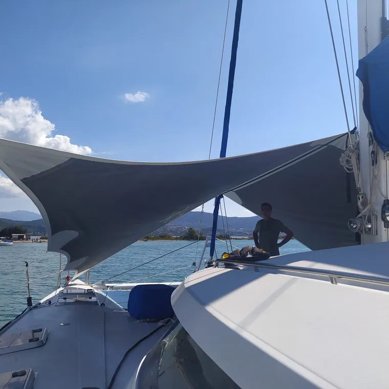 Shade sail tensioned over the foredeck of a yacht, coast behind