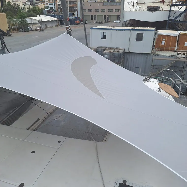 White shade sail with a logo cut into it, seen from below