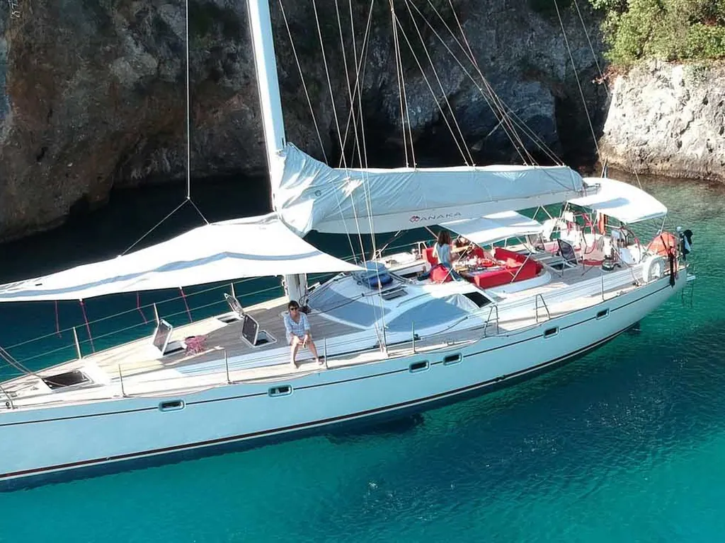 A sailing yacht at anchor in a turquoise cove under a white shade sail